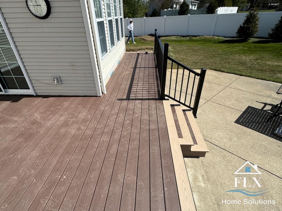Brown composite deck with black metal railing and stairs leading to patio