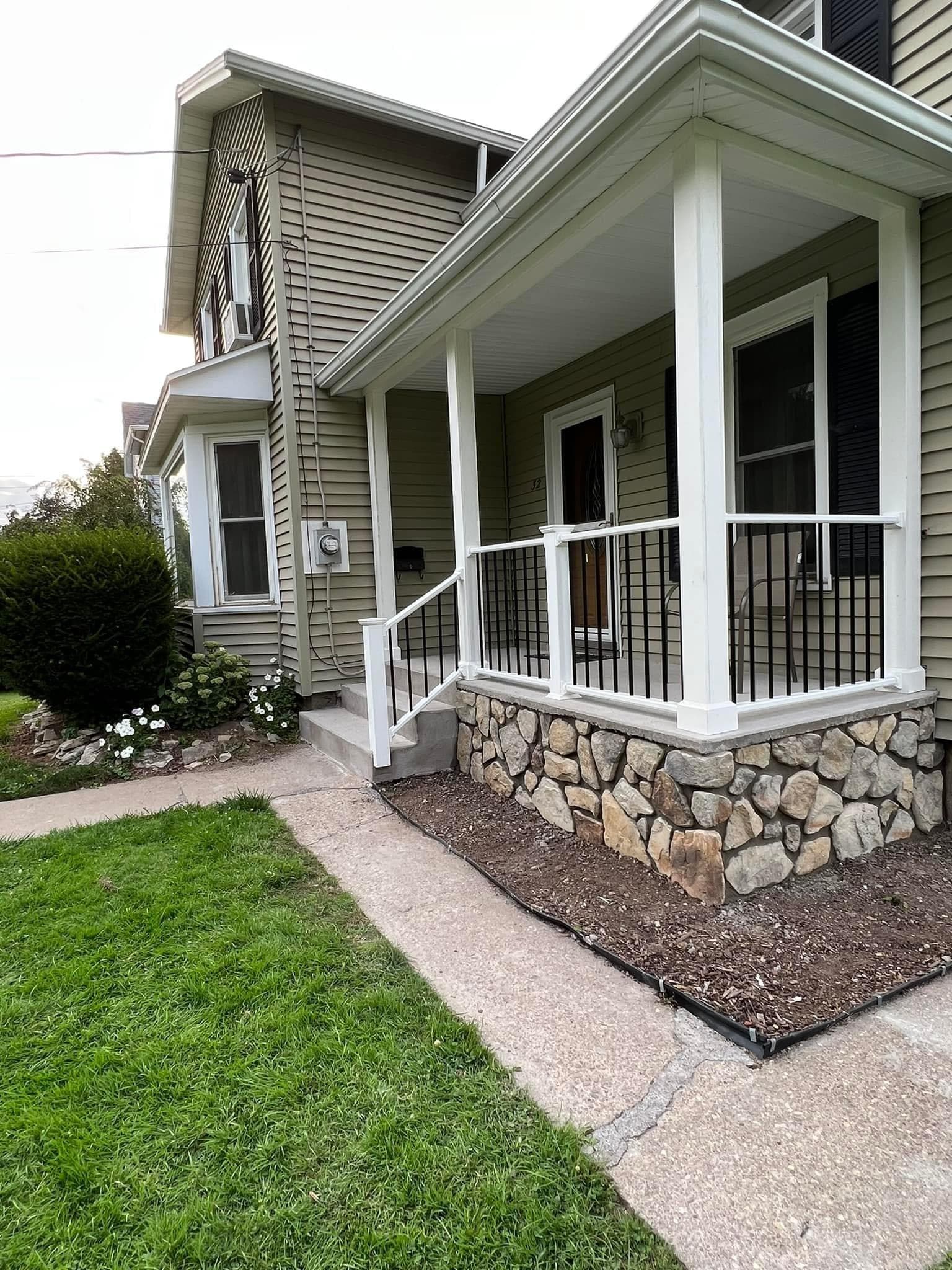 Covered front porch with white railings and stone foundation