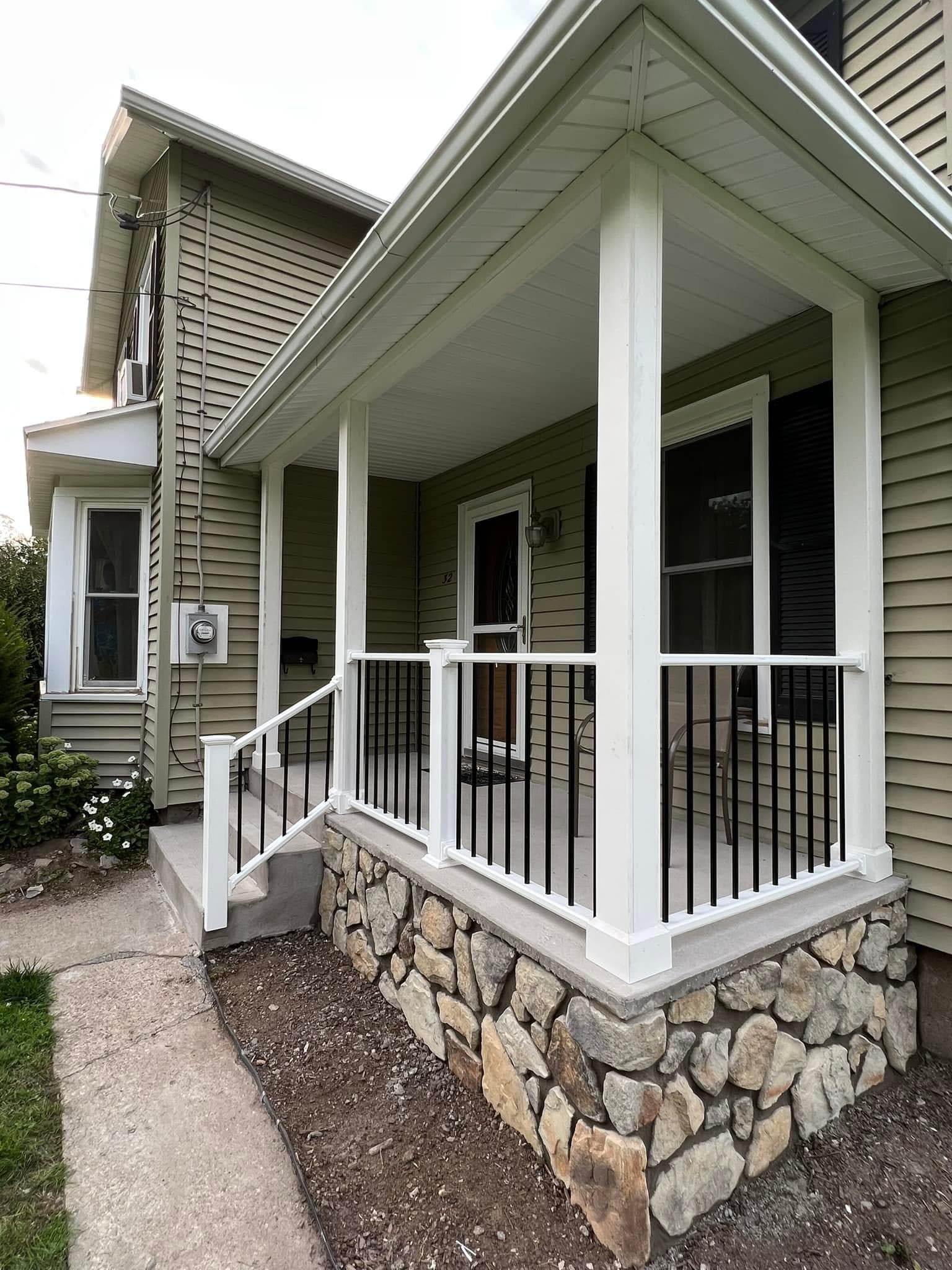 Covered front porch with white railings and stone foundation