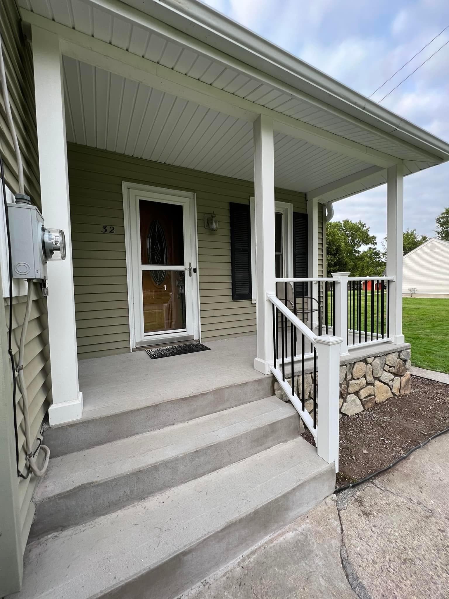White covered porch with concrete steps and black metal railings at house number 32