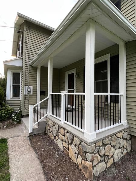 Covered porch with white railings and stone foundation on beige vinyl siding home
