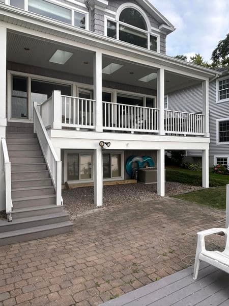 Two-story covered porch with white railings and stairs leading to paver patio