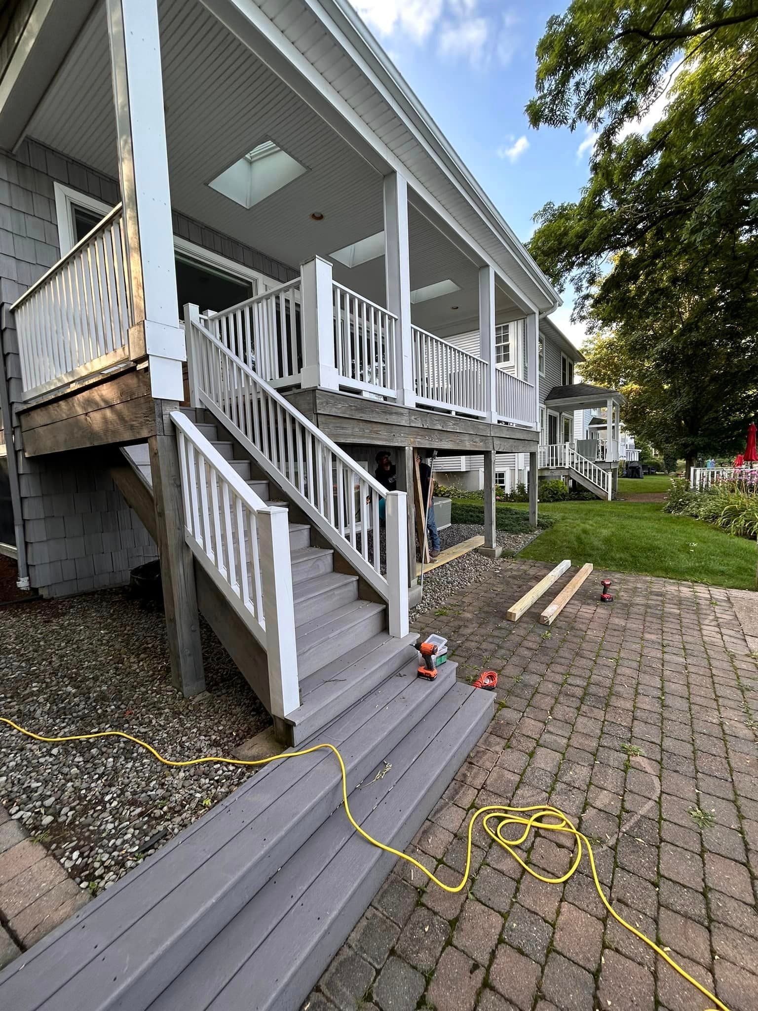 Gray house with elevated covered porch, white railings, and stairs under construction