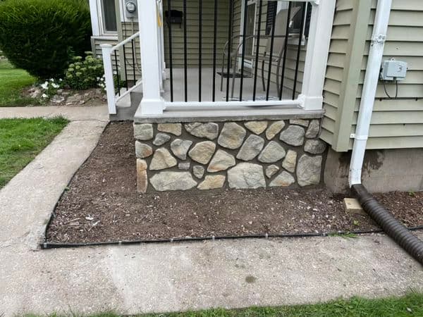 Stone foundation repair beneath screened porch with black metal railing