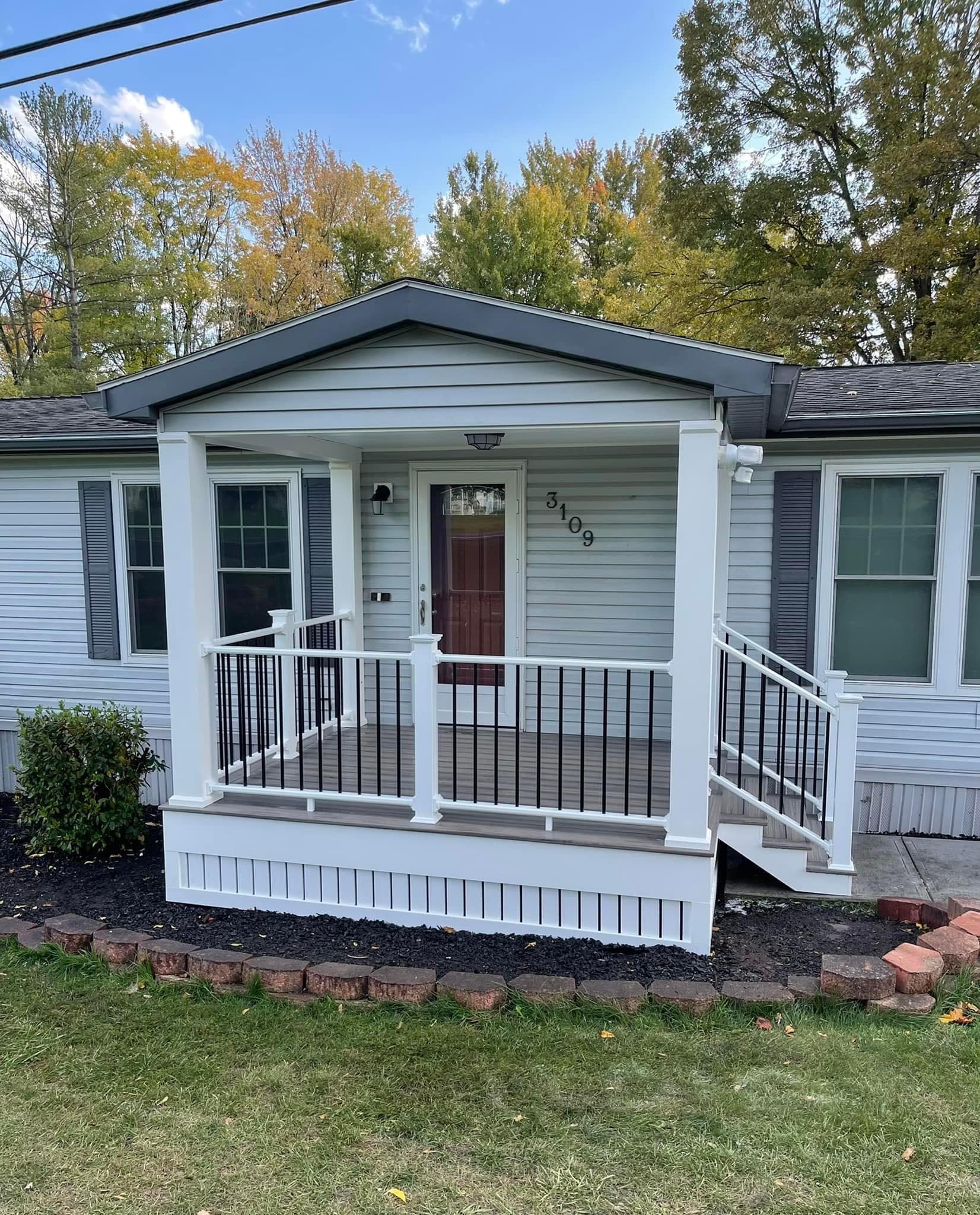 Single-story gray house with white front porch, dark railings, and burgundy door