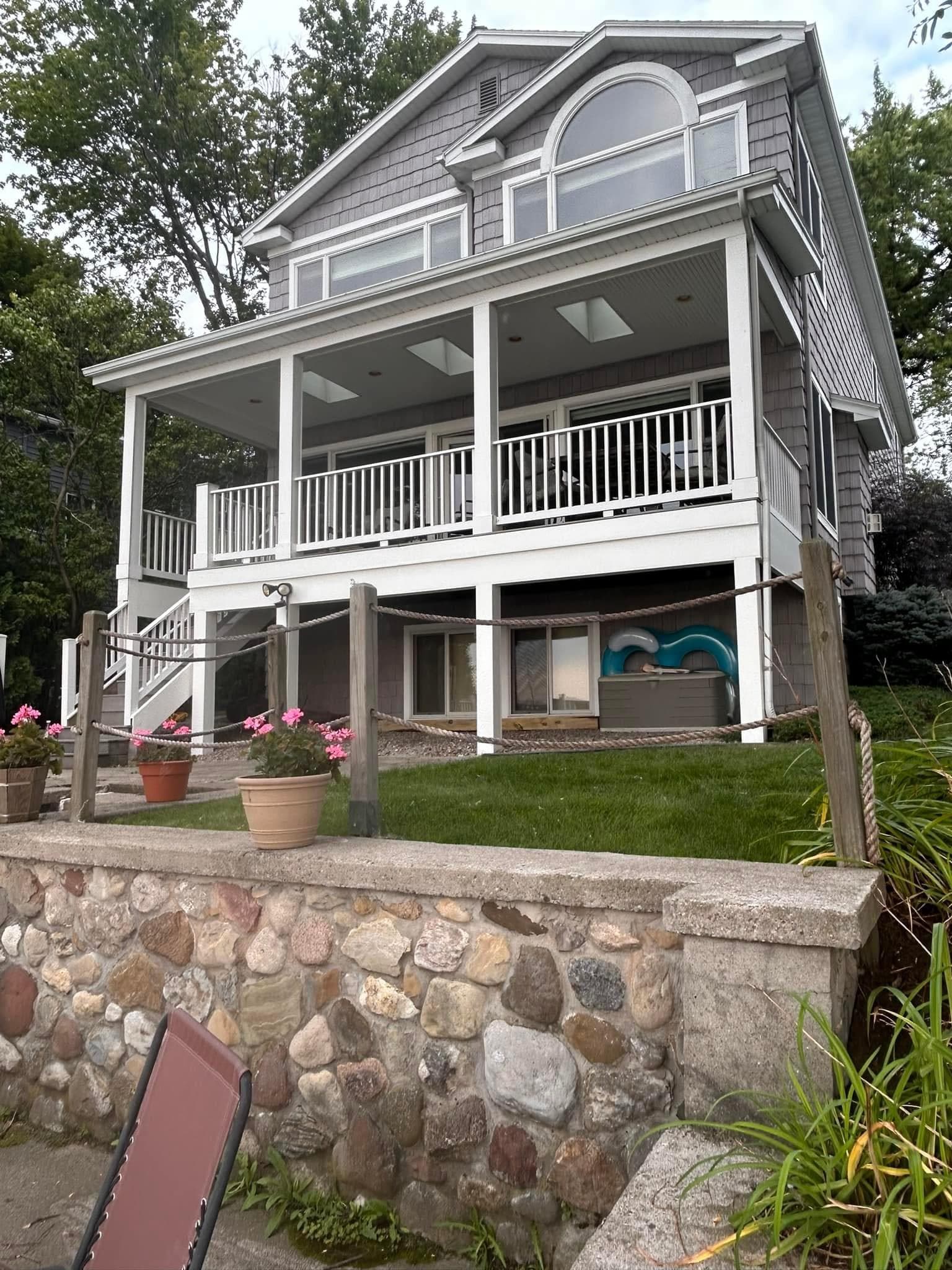 Two-story home with covered porch, white railings, and stone retaining wall