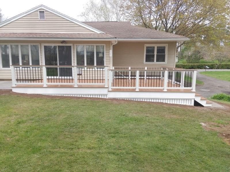 Beige ranch home with wraparound white deck featuring white and black railings