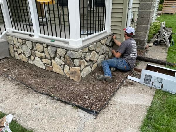 Worker installing decorative stone veneer on porch foundation