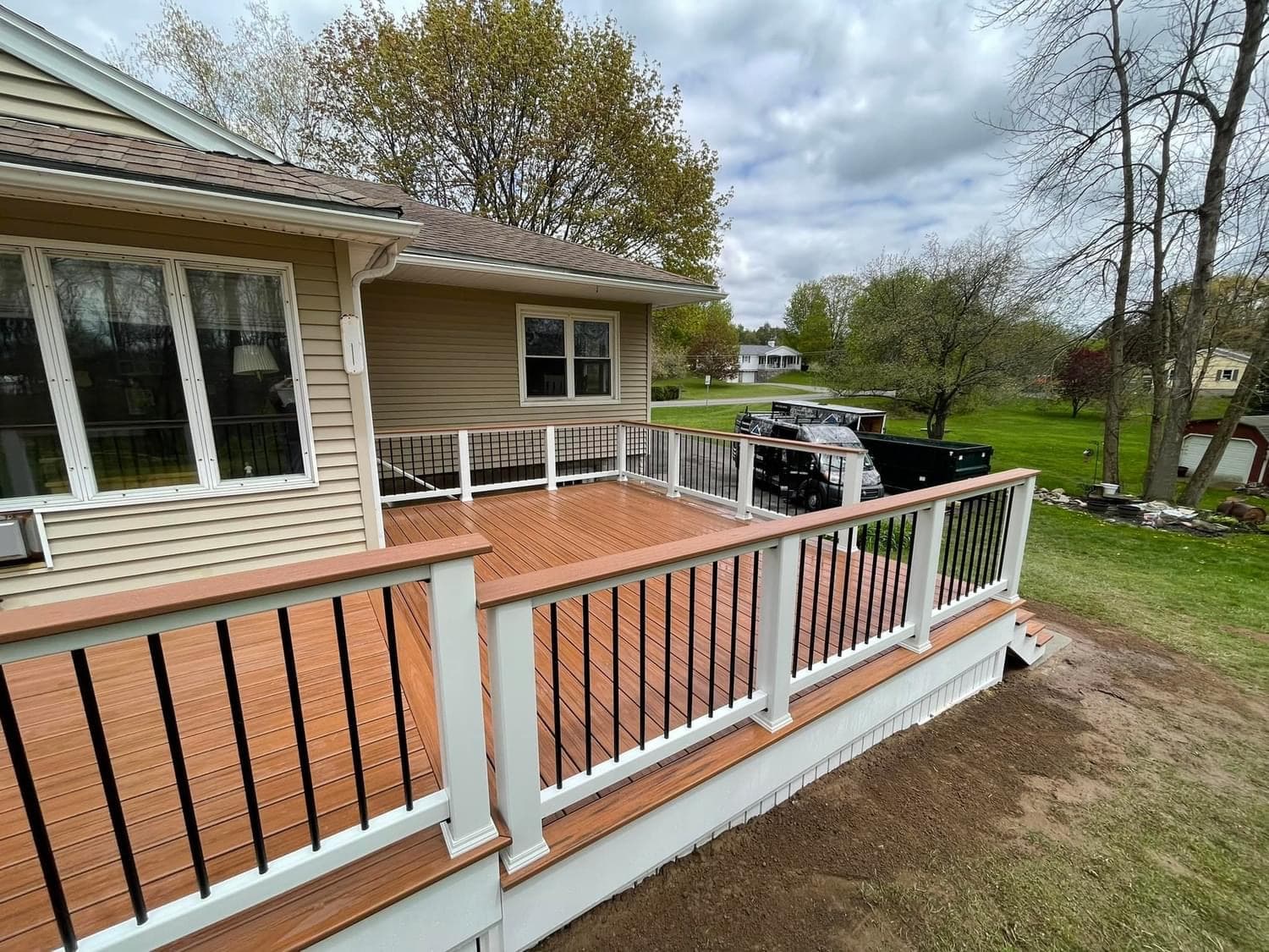 Multi-level composite deck with white posts and black metal balusters attached to beige home