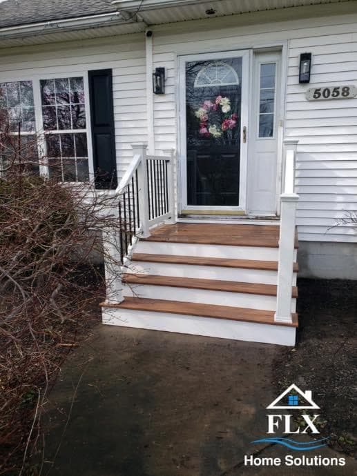 White front porch with wooden steps and black door with floral wreath
