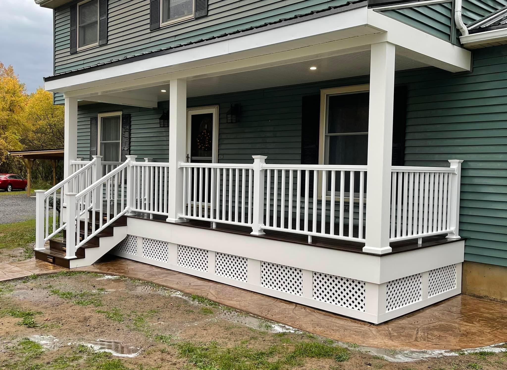 Covered front porch with white railings and lattice skirting on green house