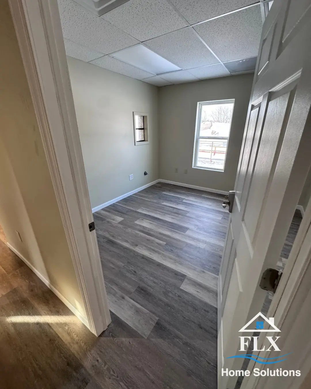 Newly finished room with window, drop ceiling, and gray vinyl plank flooring