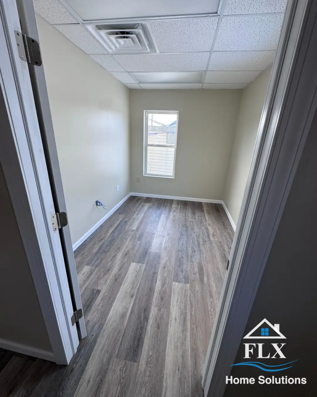 Renovated room with window, drop ceiling, and wood-tone vinyl plank flooring