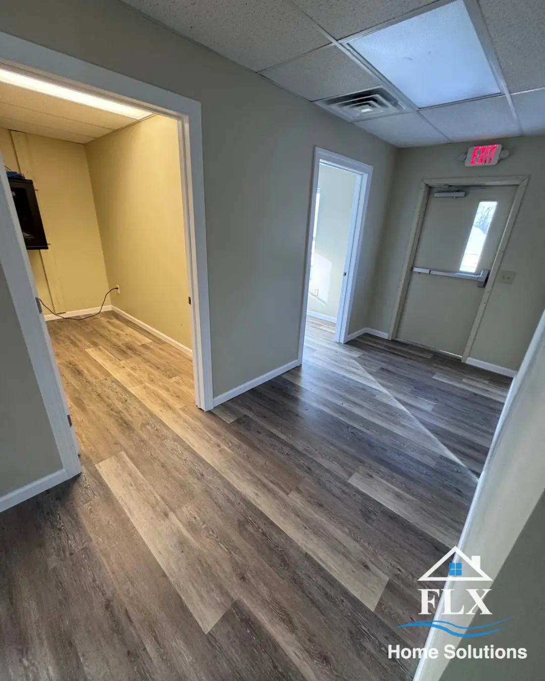 Renovated hallway with vinyl plank flooring leading to multiple rooms and exit door